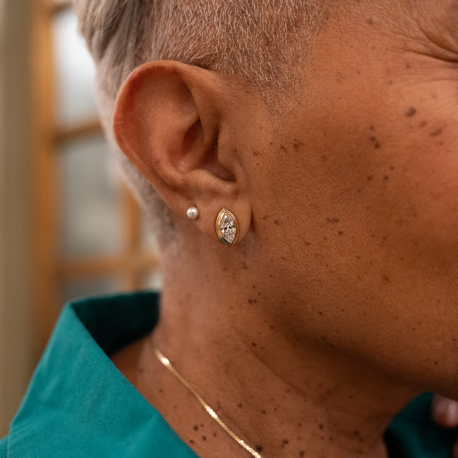 Woman's ear wearing a Sage Marquise Diamond Earring and a pearl stud and gold chain in green shirt