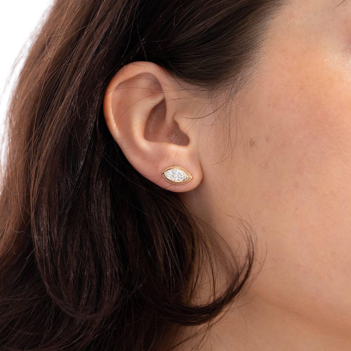 Woman's ear wearing a Sage Marquise Diamond Earring zoomed in brown hair